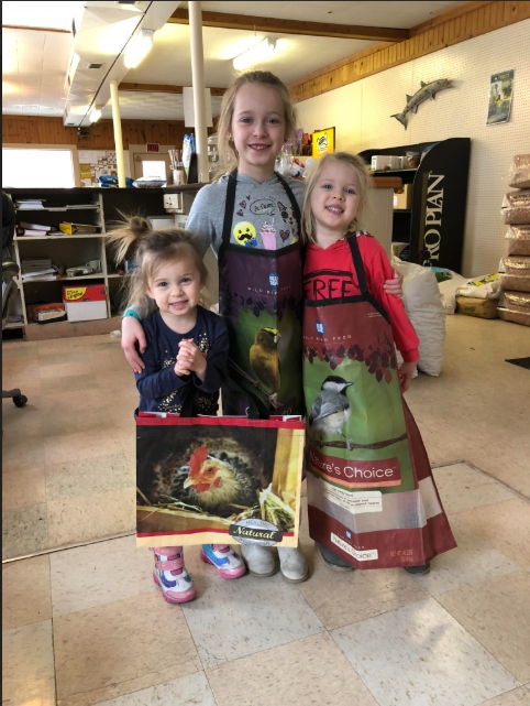 Three young girls wearing bird seed bag aprons inside Burget Mill